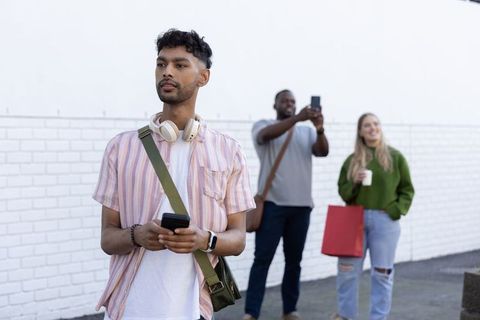 Indian man leading diverse friends on urban stroll using smartphone and headphones