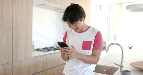 Happy Young Adult Checking Smartphone in Bright Kitchen