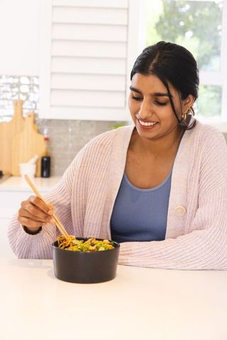 South asian woman enjoying healthy vegetable noodles at home kitchen