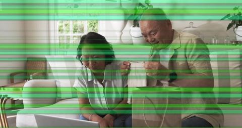Mature couple using laptop while opening gift bag in sunlit living room with green glitch
