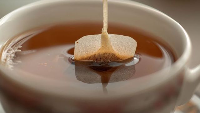 Mesh tea bag floating in amber tea close-up, steeping in white ceramic cup with reflection