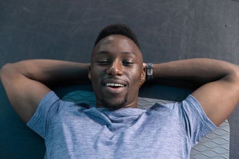 African american athlete lying on gym mats relaxing after workout with smartwatch, smiling