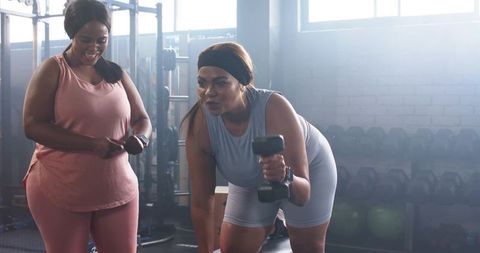 Diverse women training together doing single-arm dumbbell rows in sunlit gym