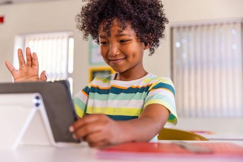 African american child using tablet for distance learning in bright classroom, smiling