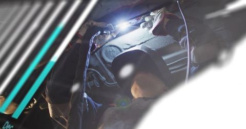 Female welder repairing vehicle underbody with welding torch and protective helmet
