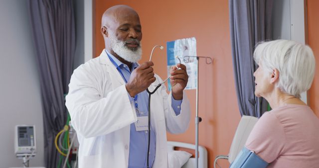 African american male doctor using stethoscope examining senior caucasian female patient at hospital. Medicine, healthcare, lifestyle and hospital concept.