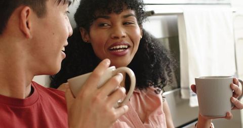 Young couple sharing morning coffee and laughing in cozy kitchen, casual home lifestyle