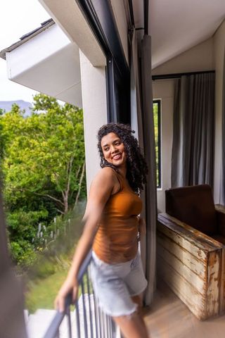 African american woman leaning on balcony railing smiling and looking left in orange top