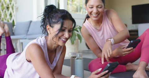 Indian and african american women sharing workout apps on smartphones during home workout