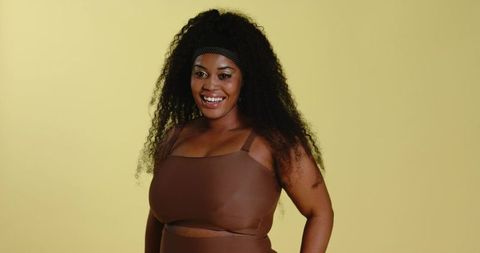 Confident smiling african american woman wearing brown activewear posing on yellow backdrop