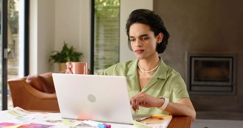 Adult male holding mug and working on laptop with color swatches in minimalist home office