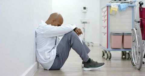 Exhausted african american clinician sitting hospital hallway near wheelchair showing burnout