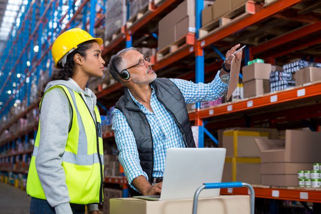 Warehouse manager and female worker interacting while using laptop in warehouse
