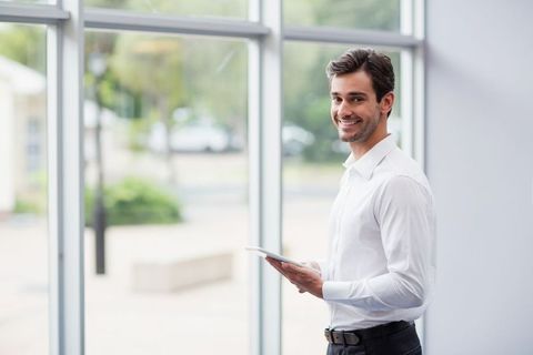Smiling Professional Holding Tablet by Office Windows