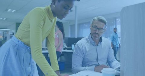 Woman leaning over papers, coworker reviewing documents and planning at open-plan office