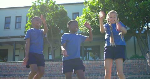 Diverse schoolchildren jumping on brick steps in blue uniforms, joyful outdoor recess