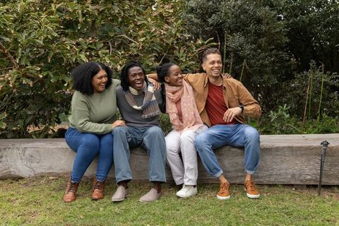 Multicultural friends laughing and sitting together on wooden bench in leafy park
