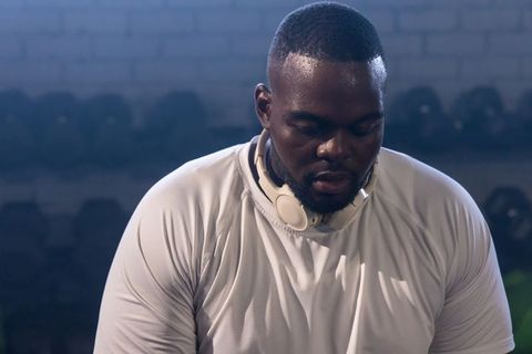 Sweating african man wearing headphones and long-sleeve shirt after weight training in gym