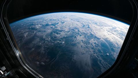 Curved earth horizon through spacecraft cupola showing atmospheric glow and cloud swirls