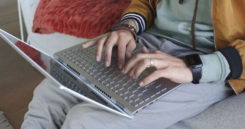 Typing on laptop on sofa wearing smartwatch and mustard jacket casual remote work