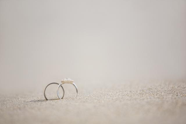 Two wedding rings are placed on the sandy beach, symbolizing love and commitment. Ideal for use in wedding invitations, engagement announcements, and romantic promotional materials.