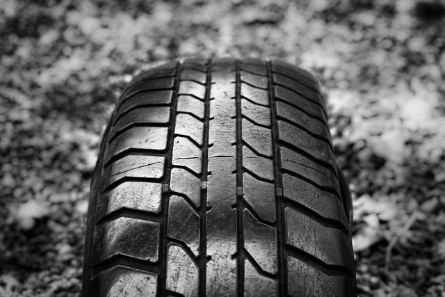 Close-up shot of a worn-out car tire showcasing intricate tread patterns in a black and white setting. Perfect for illustrating themes of vehicle maintenance, safety, and auto repair services. Useful for articles, blogs, and advertisements about tire care, road safety, or the automotive industry.