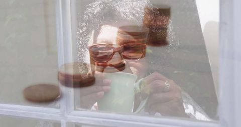 Elderly woman facing economic worry, sipping tea by foggy window