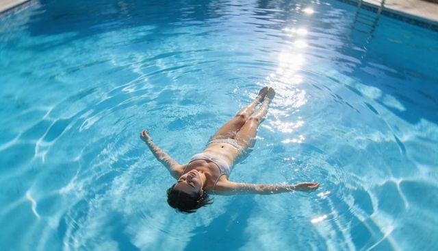 Woman floating in sunlit pool wearing white bikini, serene summer relaxation