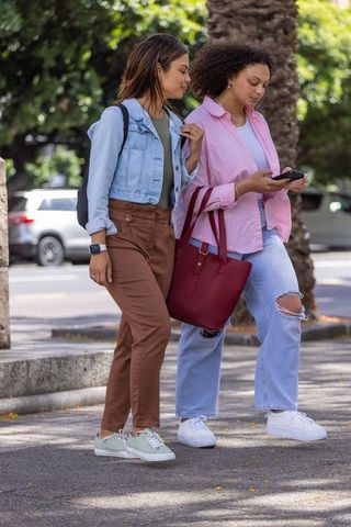 African american women walking city street checking smartphone carrying red tote bag