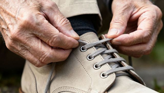 Tying shoelaces by elderly hands closeup showing wrinkled skin suede tan shoe