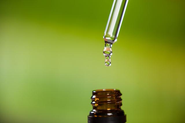 Close-up of drop of oil dripping from pipette into bottle of essential oil