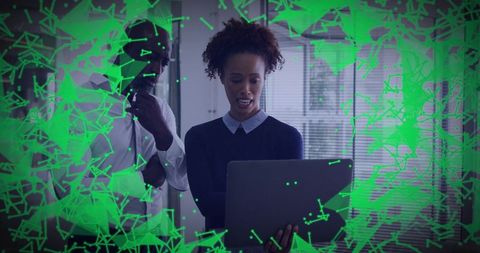 Colleagues reviewing cybersecurity alert on laptop with green digital network overlay