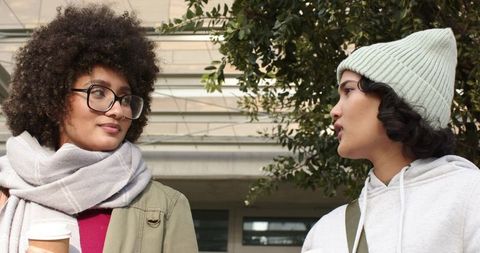 Diverse Young Women Chatting with Coffee Outside Urban Building Wearing Beanie and Scarf