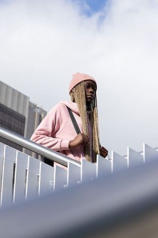 African american woman wearing pink hoodie and beanie standing on urban staircase