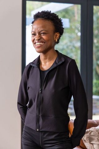 African american woman smiling and standing in black athletic jacket by sunlit glass doors