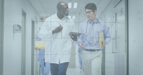 Doctors walking and reviewing tablet while carrying patient files in hospital corridor