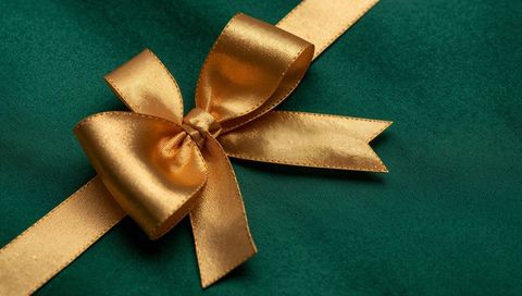 Shimmering gold satin bow resting on emerald velvet with diagonal ribbon