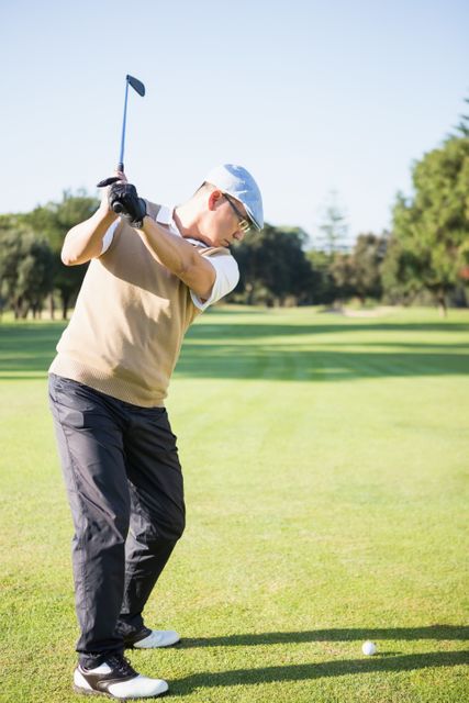 Golfer raising his golf club before taking a shot on a sunny day. Ideal for use in sports magazines, golf equipment advertisements, or articles about outdoor recreational activities.