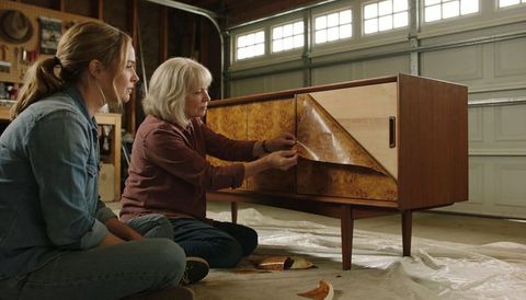 Senior woman and daughter restoring midcentury sideboard by peeling veneer in garage workshop