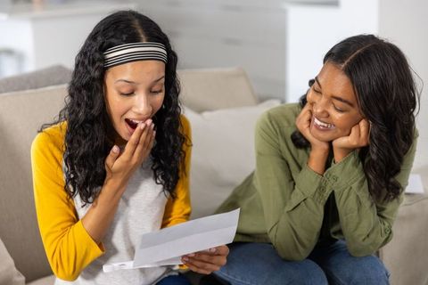 Surprised sisters reading joyful letter together on couch sharing emotional family moment