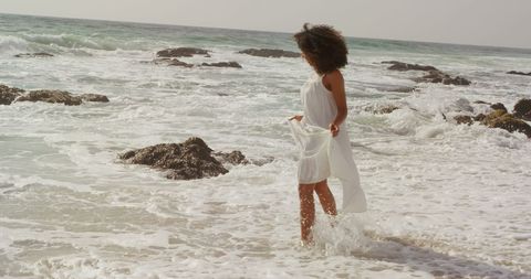 Woman in White Dress Enjoying Ocean Waves on Beach
