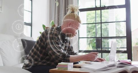 Young man with headphones studying and taking notes in bright home office workspace