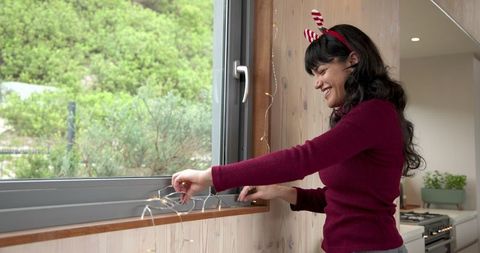 Asian Woman in Festive Attire Decorating Home with Fairy Lights