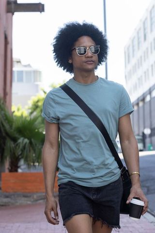 African american man walking city street wearing sunglasses holding coffee, streetwear