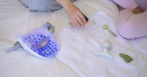 Diverse friends enjoying at-home skincare routine with led face mask, jade roller, massager