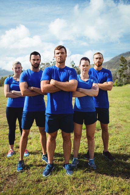 Group of fit individuals standing together with arms crossed in an outdoor boot camp on a sunny day. Ideal for use in fitness promotions, team-building advertisements, health and wellness campaigns, and motivational posters.