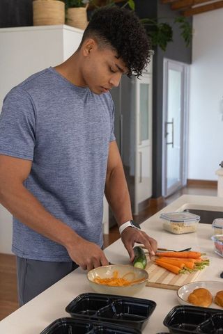 African american man prepping healthy meals at kitchen island slicing cucumber and carrots