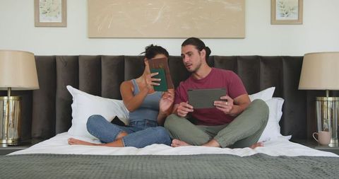 Happy Couple Enjoying Relaxed Time with Digital Tablets on Bed
