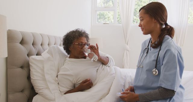 Nurse assisting senior woman in bed as she takes medication with a glass of water. This image can be used for healthcare advertisements, elderly care services promotions, medical articles, nursing home brochures, and patient care information.