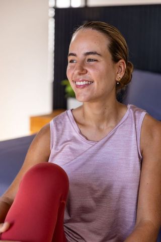 Smiling woman relaxing on sofa in pink top and red leggings, home wellness lifestyle